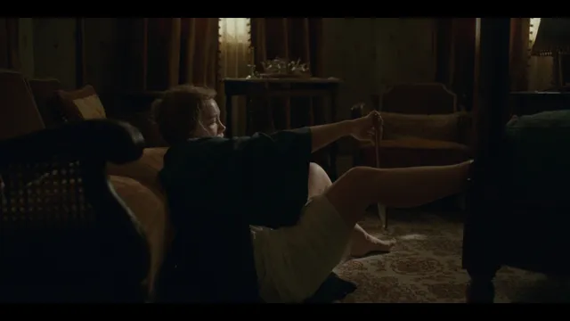 Florence Pugh sitting barefoot with legs raised in a screen scene.