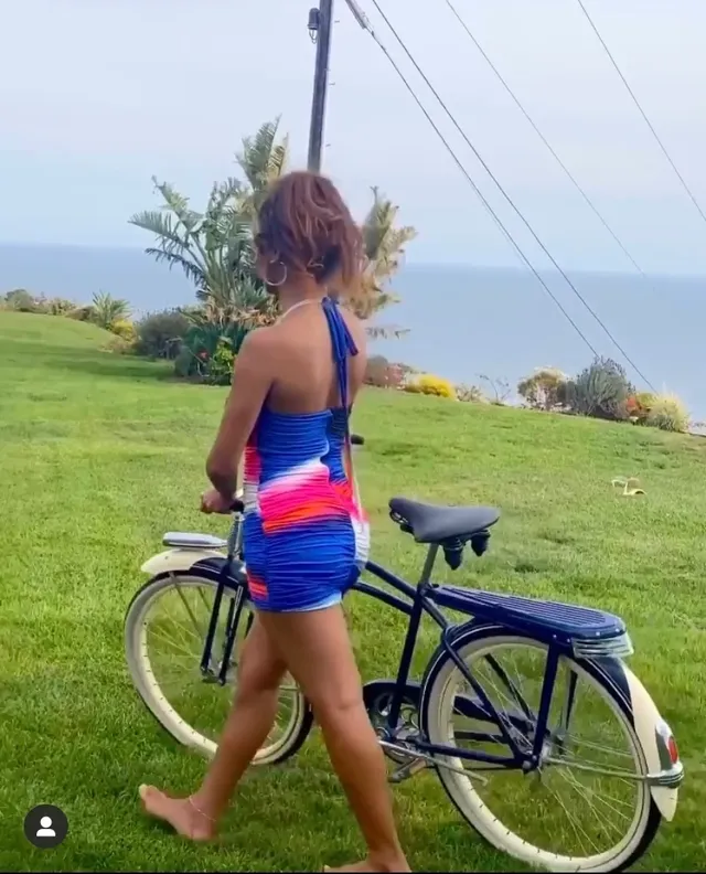 Sierra Capri walking barefoot beside a bicycle in a colorful dress.