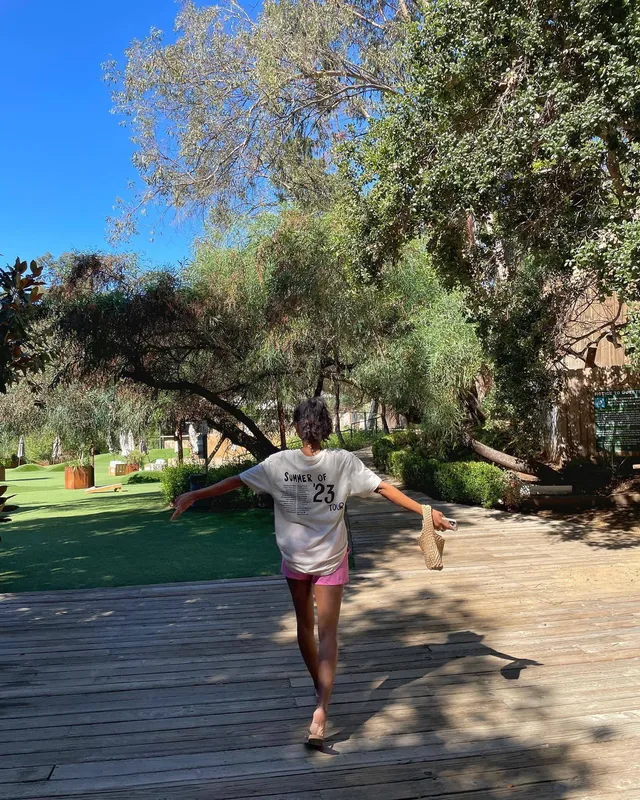 Greta Onieogou standing barefoot outdoors in a grey T-shirt and pink shorts.