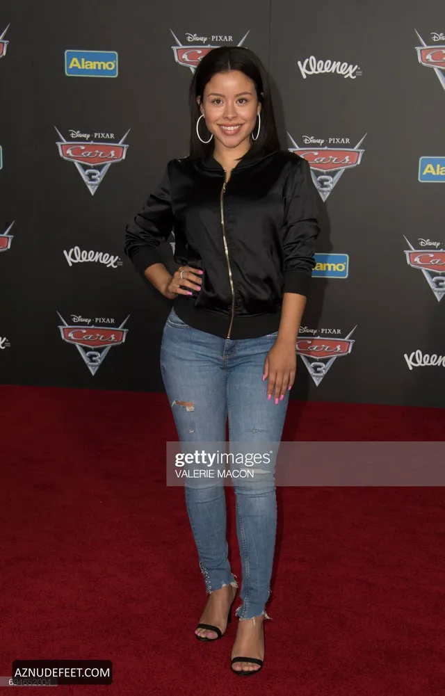 Cierra Ramirez in a black jacket, jeans and heeled sandals on a premiere carpet.