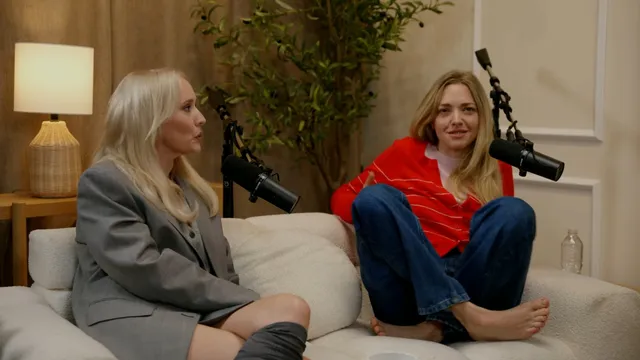 Amanda Seyfried sitting barefoot in jeans on a couch during an interview.