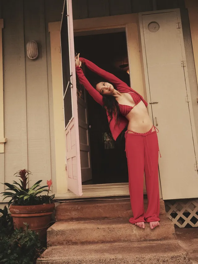Jennie Kim stretching barefoot in a doorway wearing a red outfit.