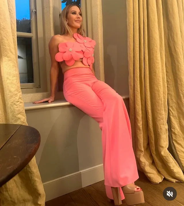 Ellie Goulding sitting beside a window in pink trousers and platform heels.
