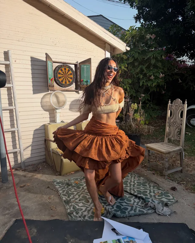 Shay Mitchell posing indoors in a brown skirt and pale top.