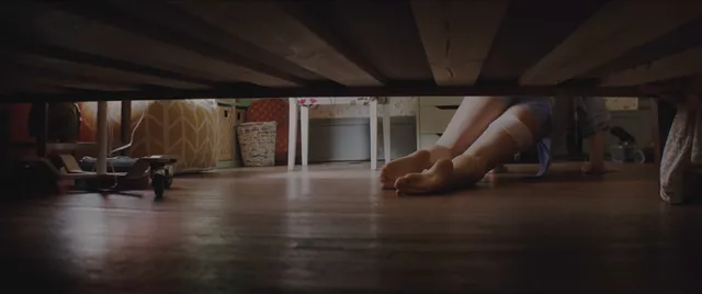Chloë Grace Moretz with bare feet extended below a bed in a screen image.