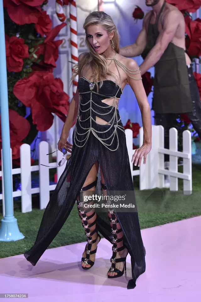Paris Hilton wearing a black dress and tall strappy sandals at an event.