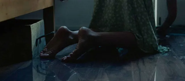 Jodie Comer sitting in a dimly lit screen scene in a green dress.