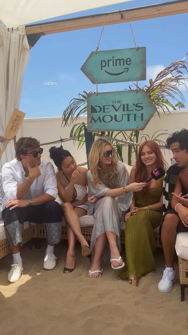 Kathryn Newton sitting with a group outdoors in a silver dress and heels.