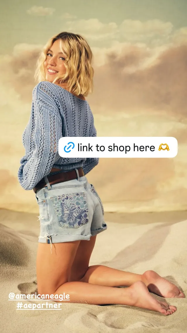 Sydney Sweeney: kneeling barefoot on sand in a denim outfit.