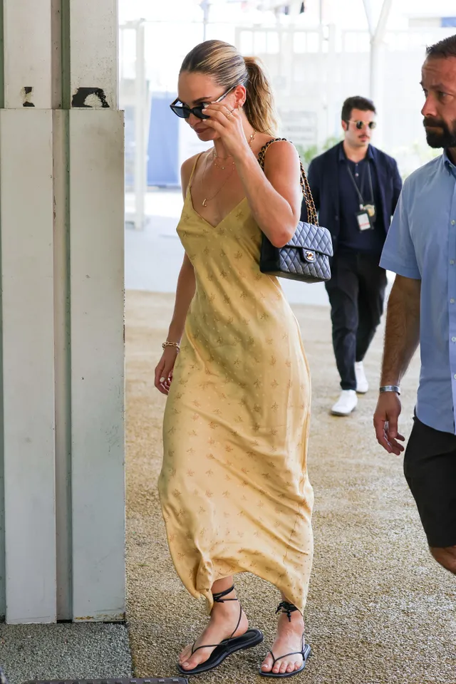 Lily James walking outdoors in a yellow dress and flat sandals.