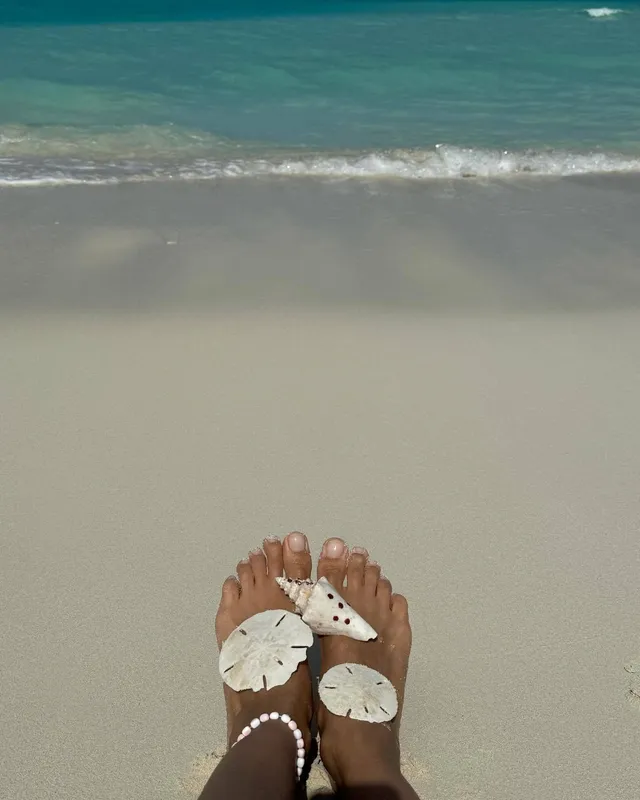 Irina Shayk bare feet with shells by the shoreline.