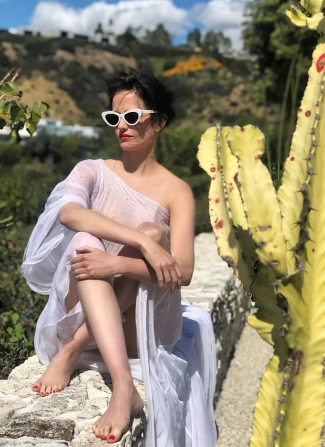 Eva Green seated beside cactus plants in a pale cover up.