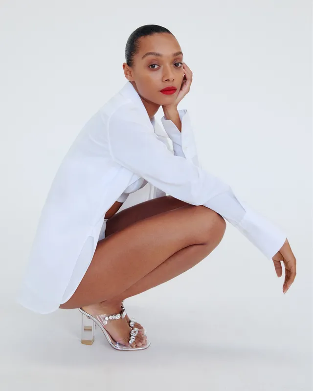 Sophie Wilde crouching in a white shirt and embellished heeled sandals.