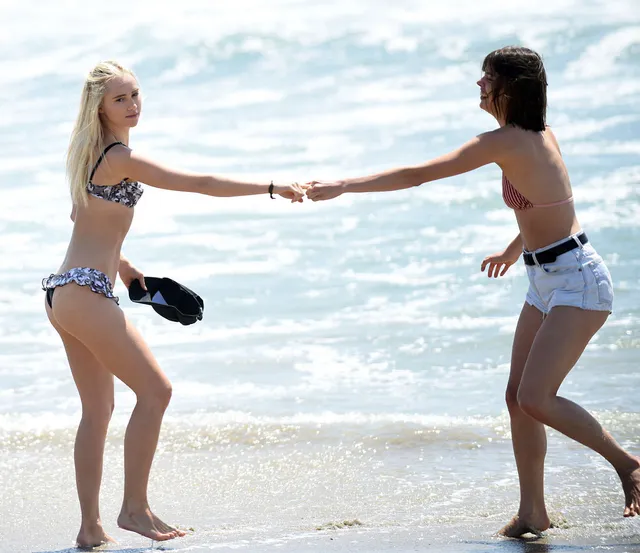 Suki Waterhouse holding hands with a companion in the surf.