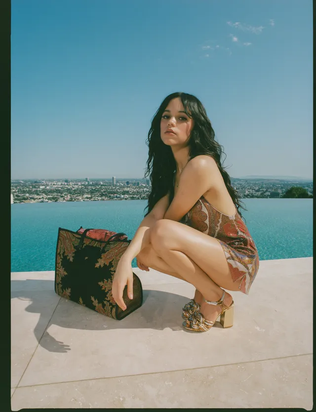 Jenna Ortega crouching beside a swimming pool in a patterned outfit and heels.