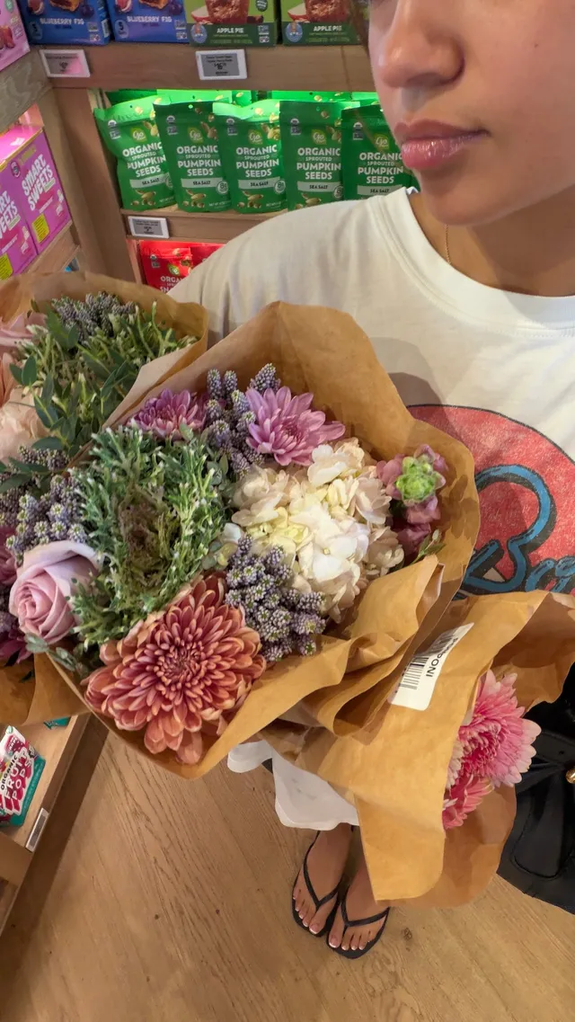 Madison Bailey holding a bouquet while wearing flat sandals.