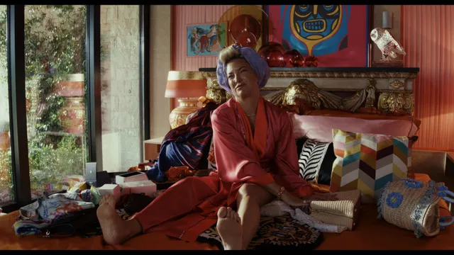 Kate Hudson sitting on patterned cushions in a red outfit.