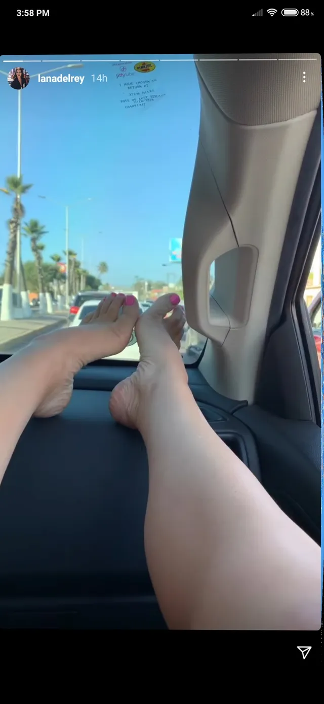 Lana Del Rey resting her bare feet on a car dashboard.