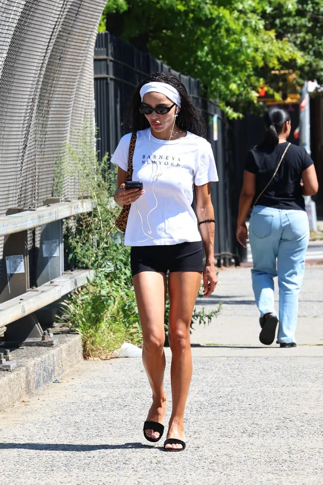 Zoë Kravitz walking on a sidewalk in a white shirt and black shorts.