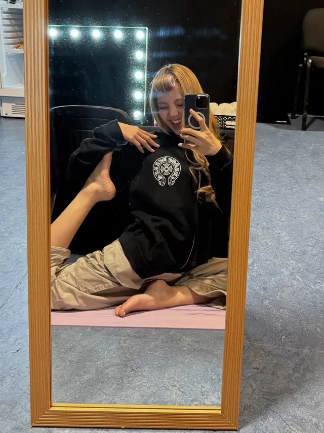 Lisa (Lalisa Manobal) sitting barefoot on a bed while taking a mirror photograph.