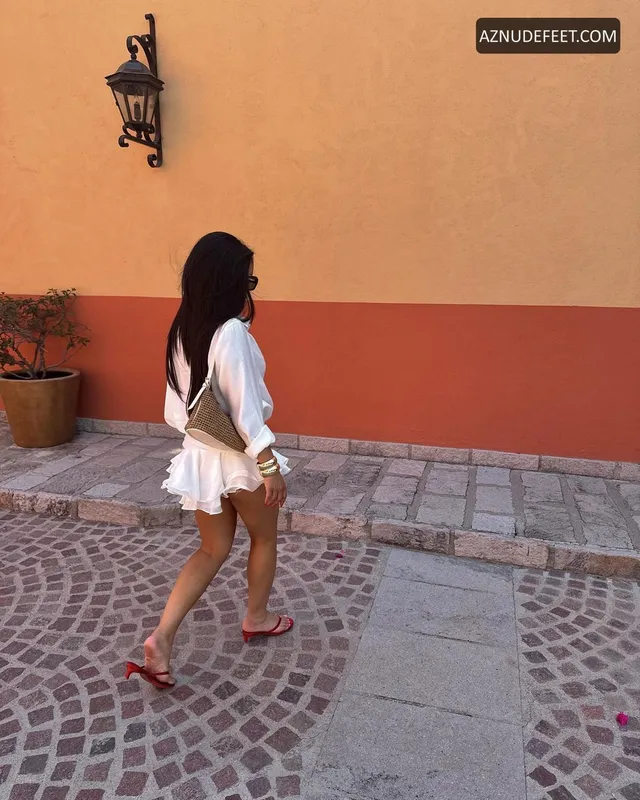 Cierra Ramirez in a white shirt and shorts with flat sandals on a cobbled street.