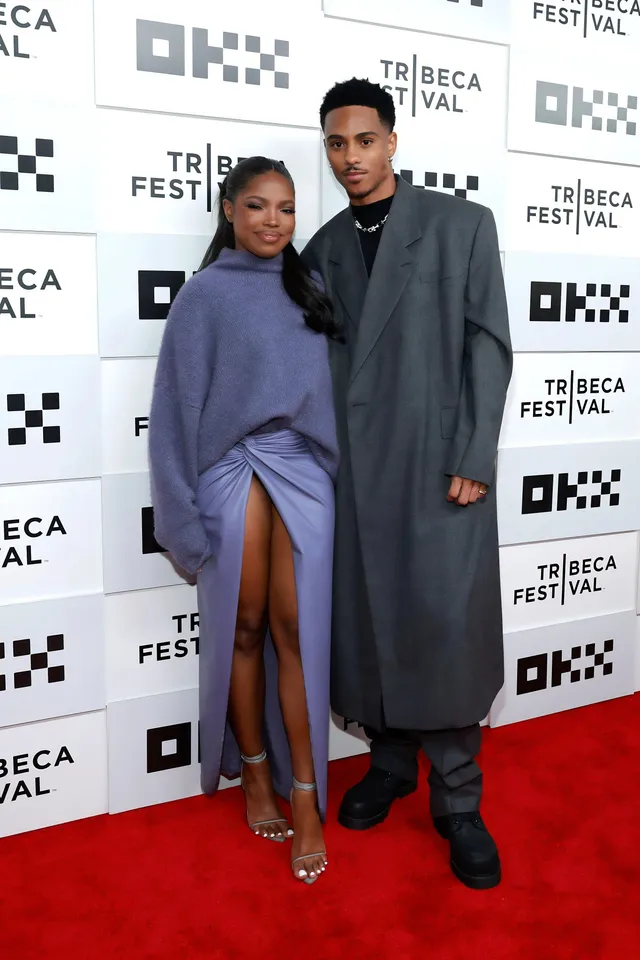 Ryan Destiny posing beside a man in a lavender dress and clear heels.