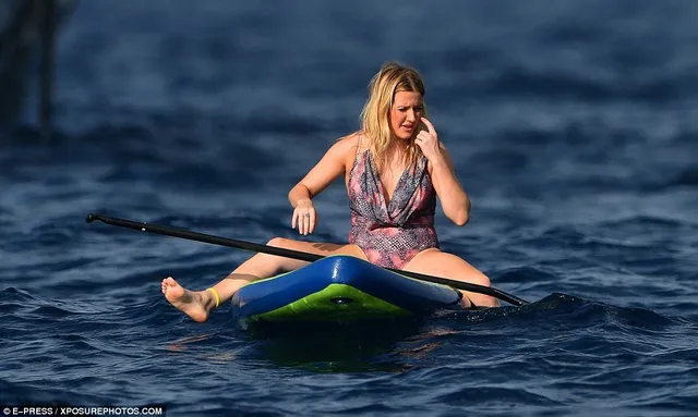 Ellie Goulding sitting barefoot on a paddleboard at sea.