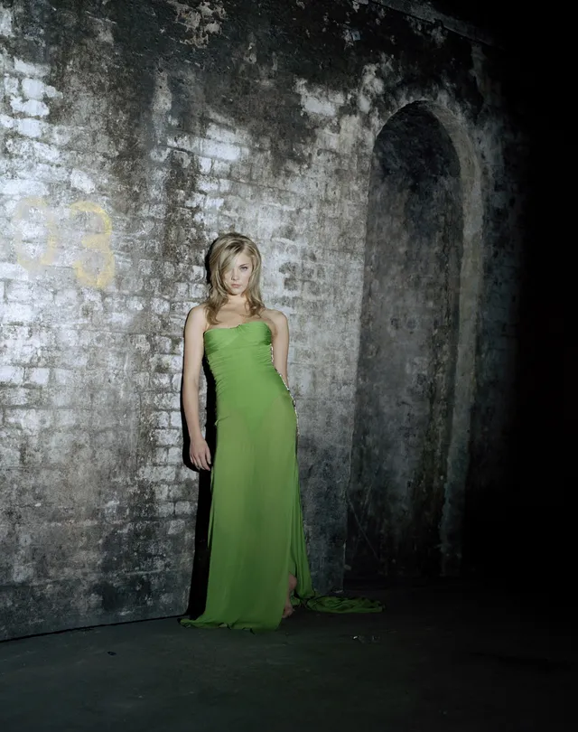Natalie Dormer posing in a long green gown beside a stone wall.