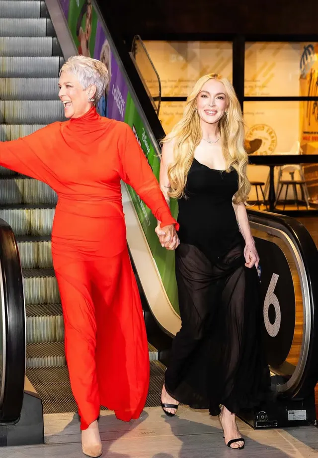 Lindsay Lohan standing in a black dress beside another woman in red.