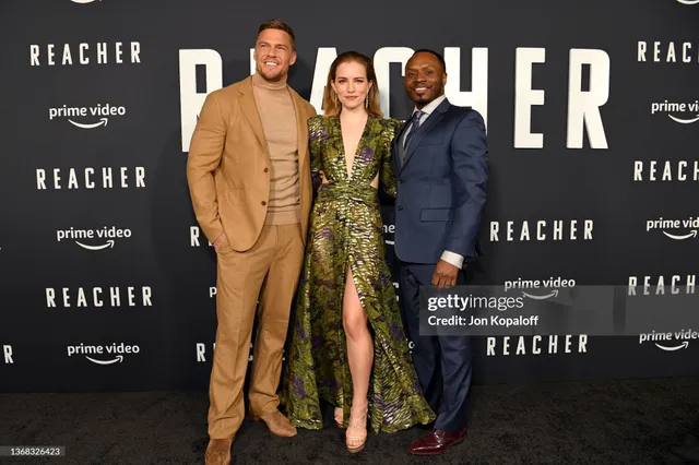 Willa Fitzgerald posing with cast members in a patterned gown and heels.