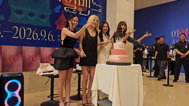 Rosé leaning toward a cake with BLACKPINK members while wearing black clothing and heels.