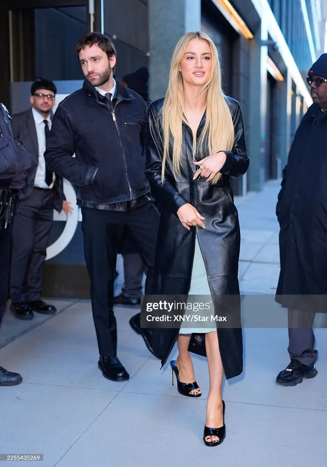 Grace Van Patten walking beside a man in a black leather dress and heels.