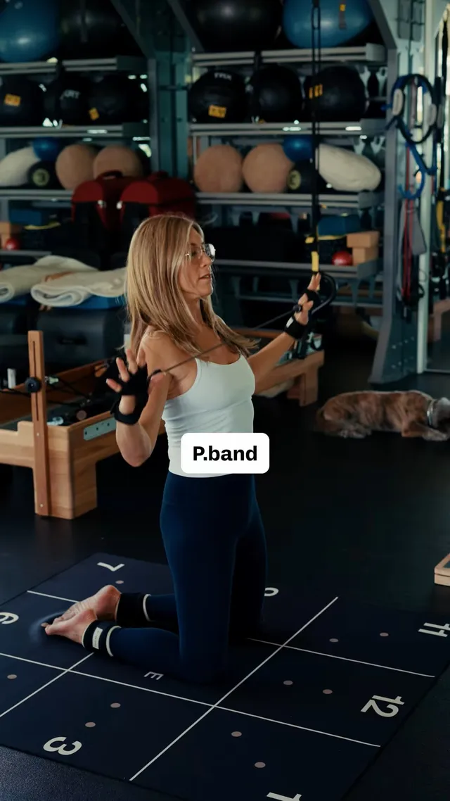 Jennifer Aniston kneeling barefoot on a gym floor during training.