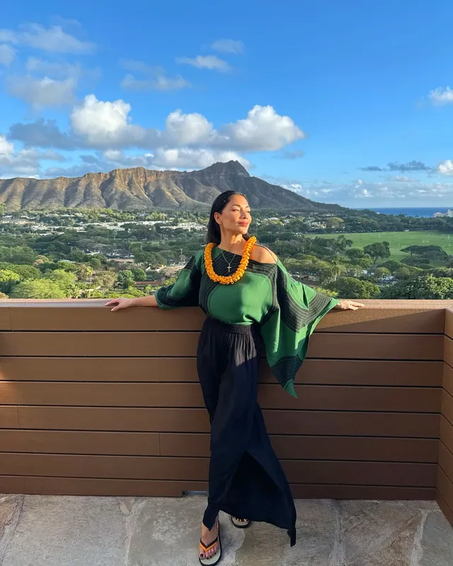 Nicole Scherzinger sitting barefoot on a terrace overlooking mountains.
