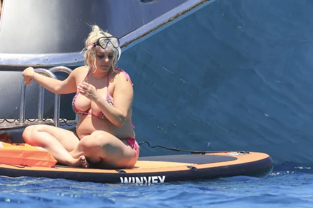 Bebe Rexha sitting barefoot on a paddleboard.
