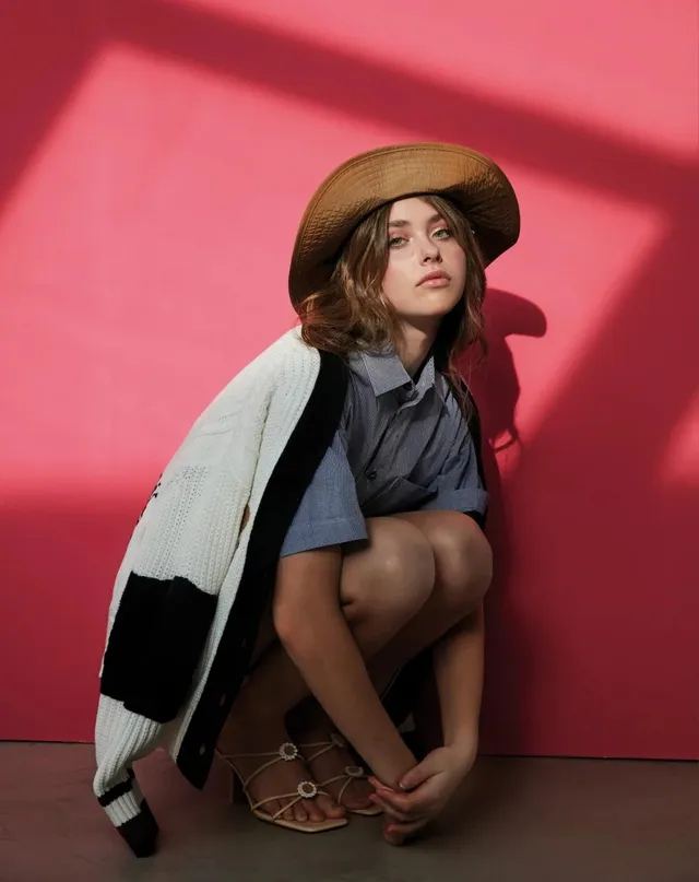 Nicole Wallace crouching in a jacket, skirt and tan flat sandals for a portrait.