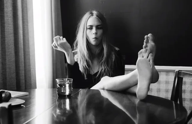 Cara Delevingne sitting at a table with her feet raised.