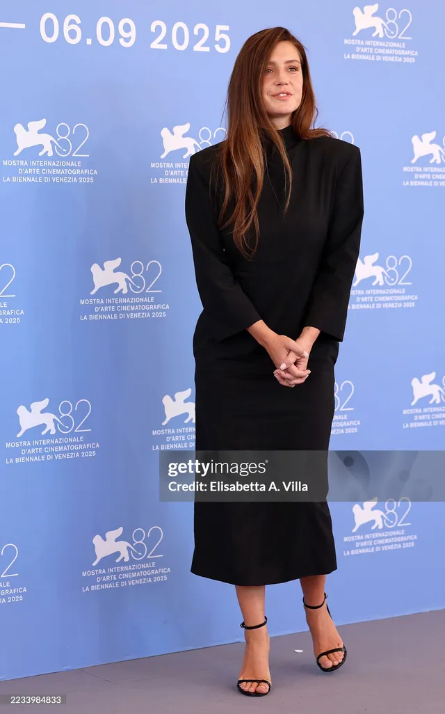 Adèle Exarchopoulos posing against a blue festival wall in a black dress.