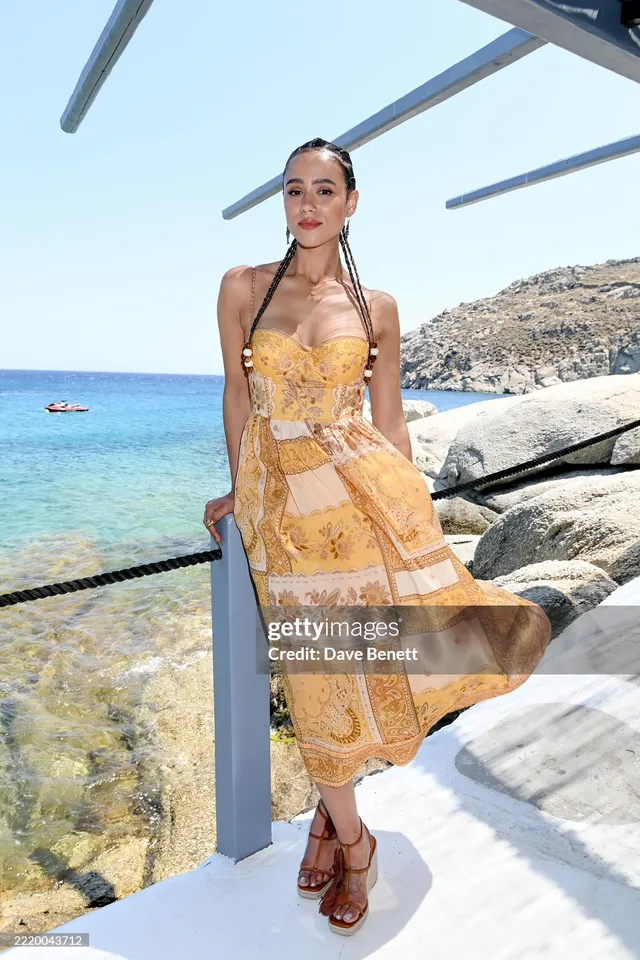 Nathalie Emmanuel posing beside the sea in a yellow dress.