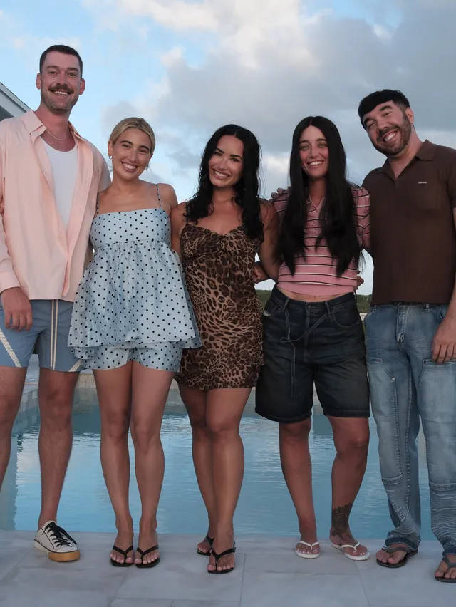 Demi Lovato posing with a group in a dark dress and flip-flops.