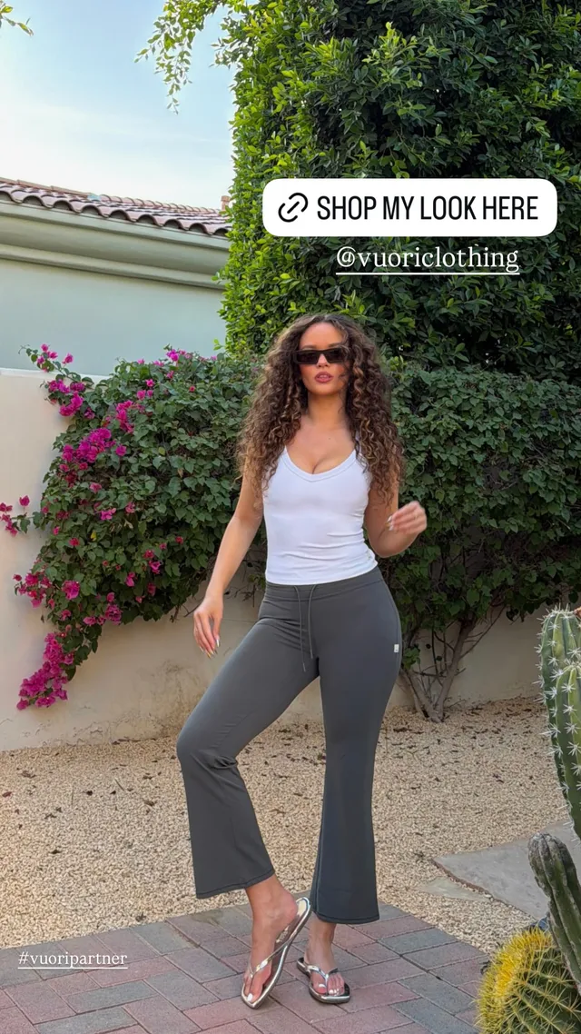 Madison Pettis posing in a white top, grey trousers and metallic flat sandals.