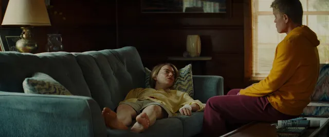 Emma Stone reclining barefoot on a sofa while another person sits nearby.
