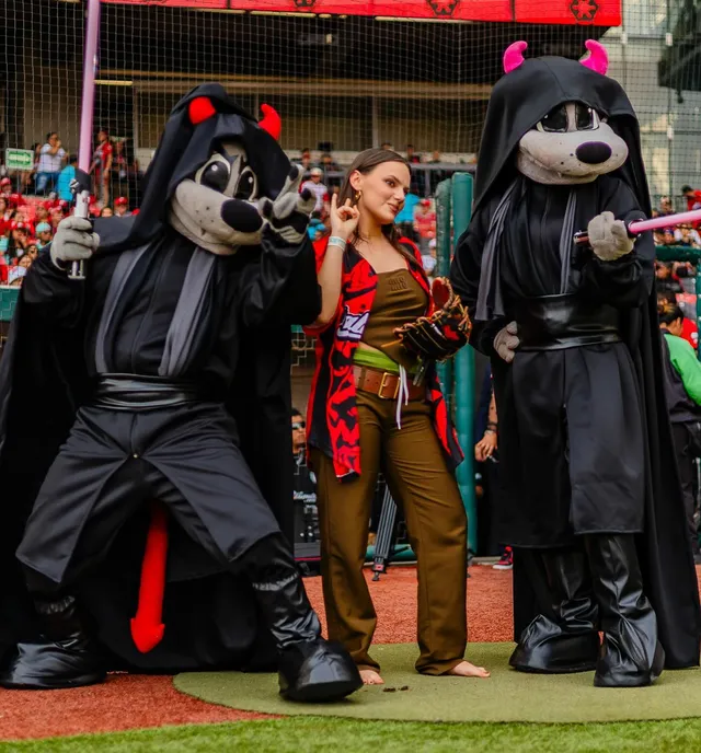 Dafne Keen posing barefoot between two costumed baseball mascots.