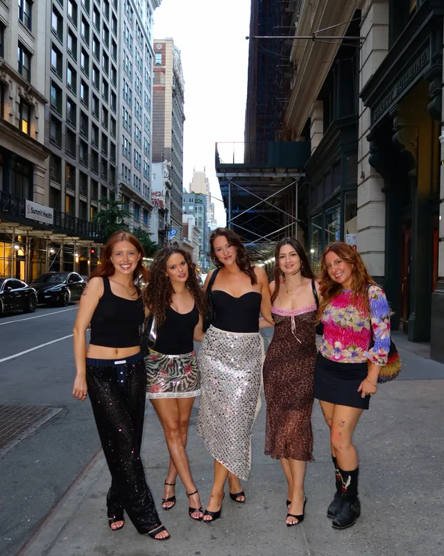 Madison Pettis posing with friends on a city sidewalk in a long silver skirt and black heels.
