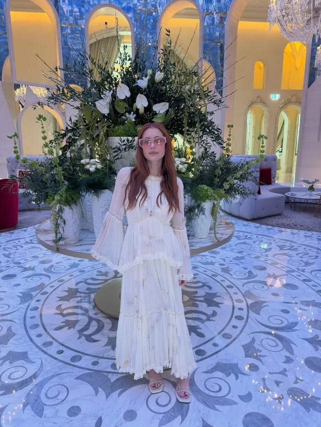Emma Roberts posing in a cream dress in an ornate hall.