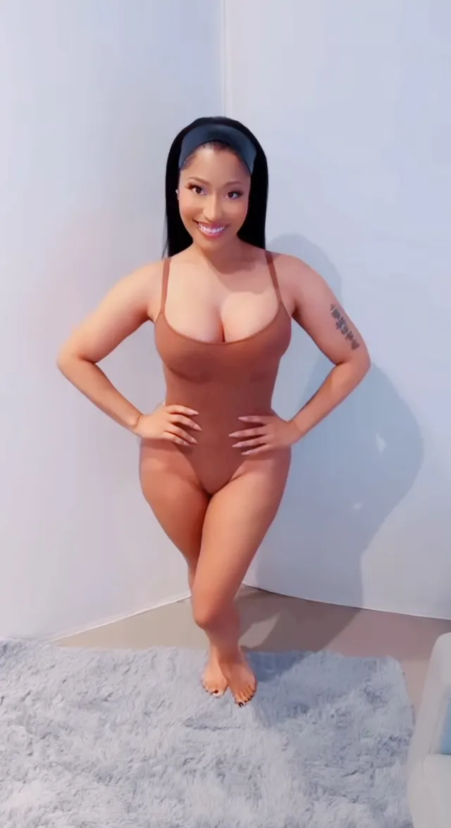 Nicki Minaj standing barefoot on a pale rug in a studio portrait.