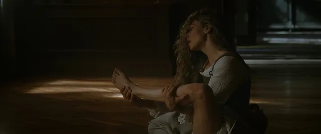 Amanda Seyfried sitting barefoot in a dimly lit screen image.