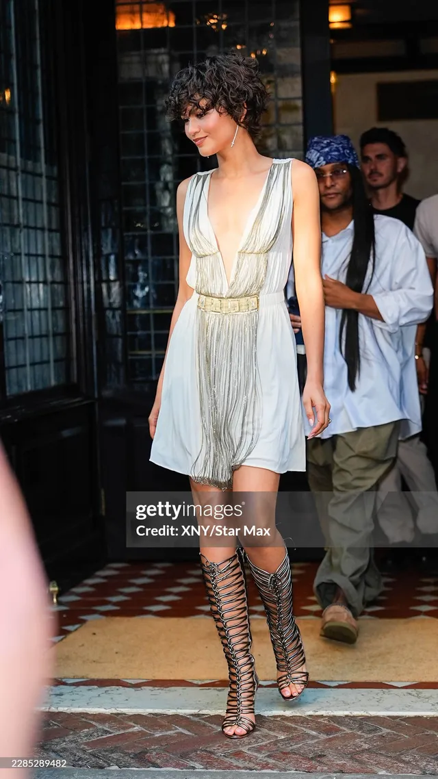 Zendaya standing among guests in a white dress.