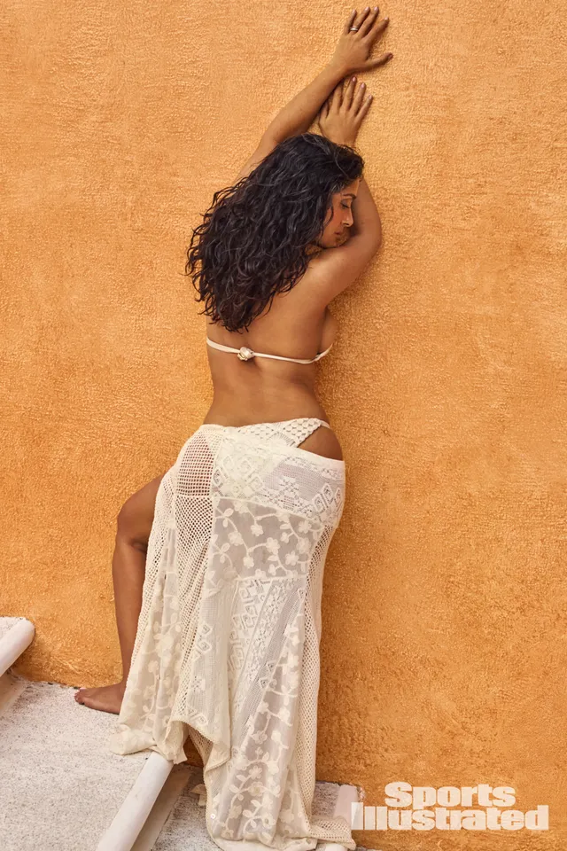 Salma Hayek standing against an orange wall in a white lace skirt.