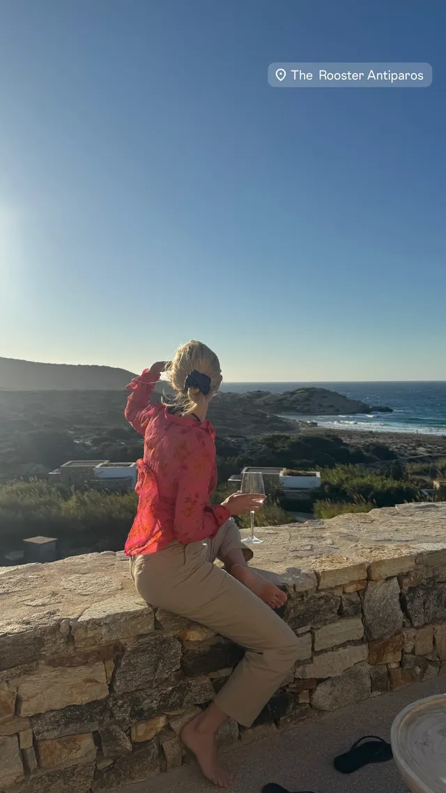AnnaSophia Robb sitting on a stone wall overlooking the coast.